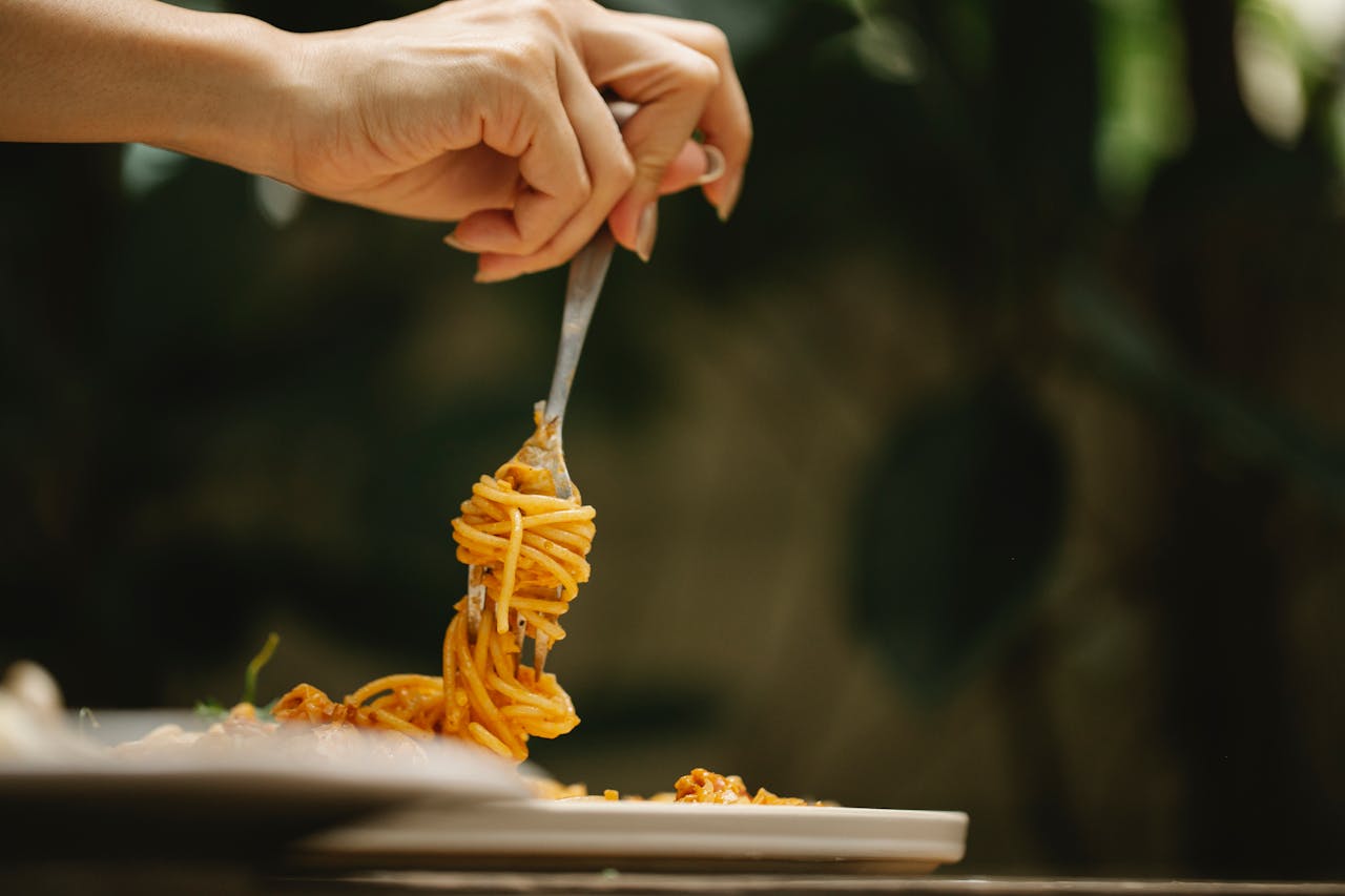 Crop anonymous female rolling delicious spaghetti with tomato sauce on fork during dinner in restaurant